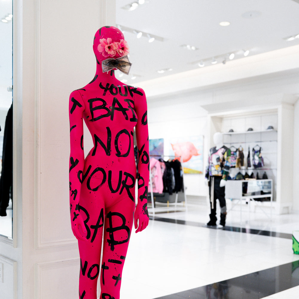 Person wearing a bright pink bodysuit with black text in a store setting