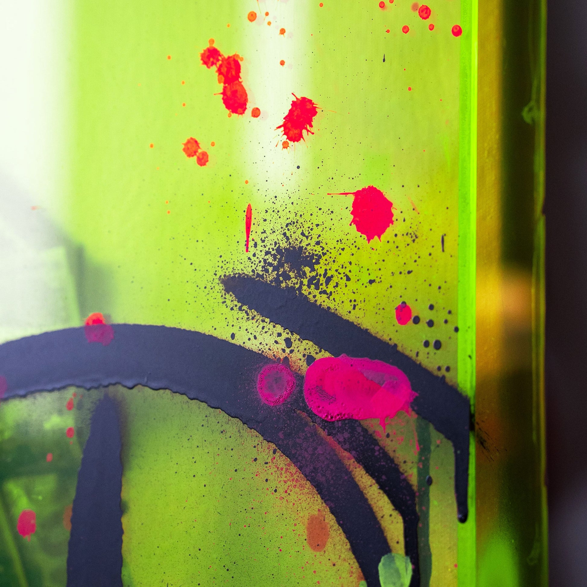 Close-up of a colorful abstract art piece with red, black, and pink splashes on a green background.
