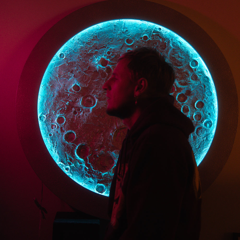 Person standing in front of a large moon-like structure with a blue glow.