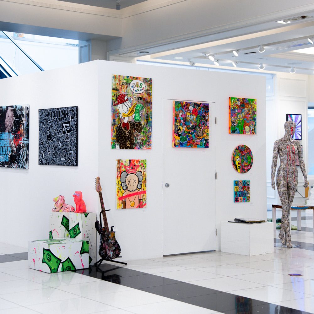Modern art gallery with colorful paintings and sculptures on a white wall.