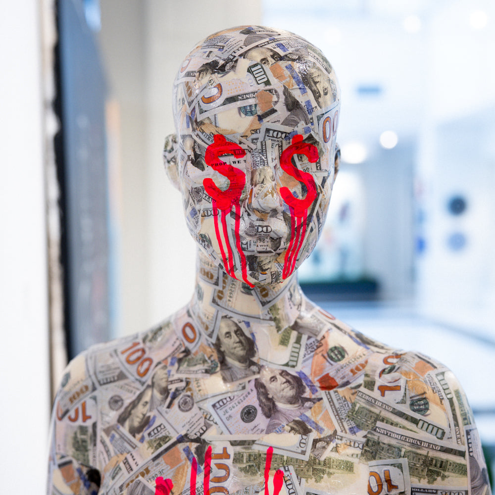 Mannequin covered in dollar bills with red dollar signs on a blurred indoor background