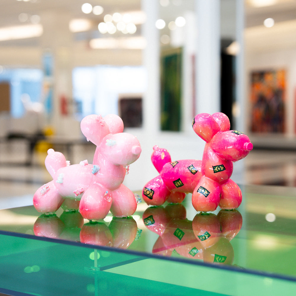 Pink balloon dog sculptures on a reflective surface with a blurred indoor background