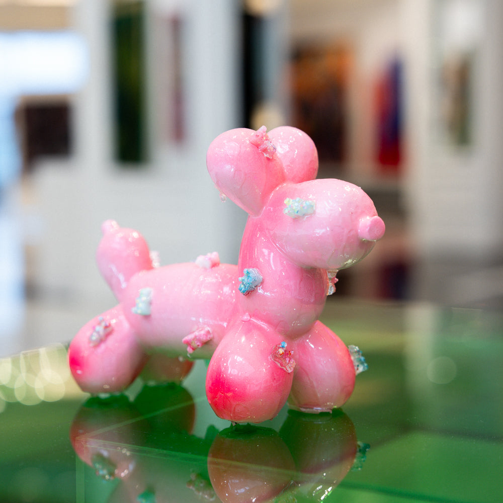 Pink balloon dog sculpture on a reflective surface with a blurred background