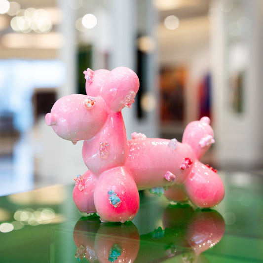 Pink balloon dog sculpture on a reflective surface with a blurred indoor background