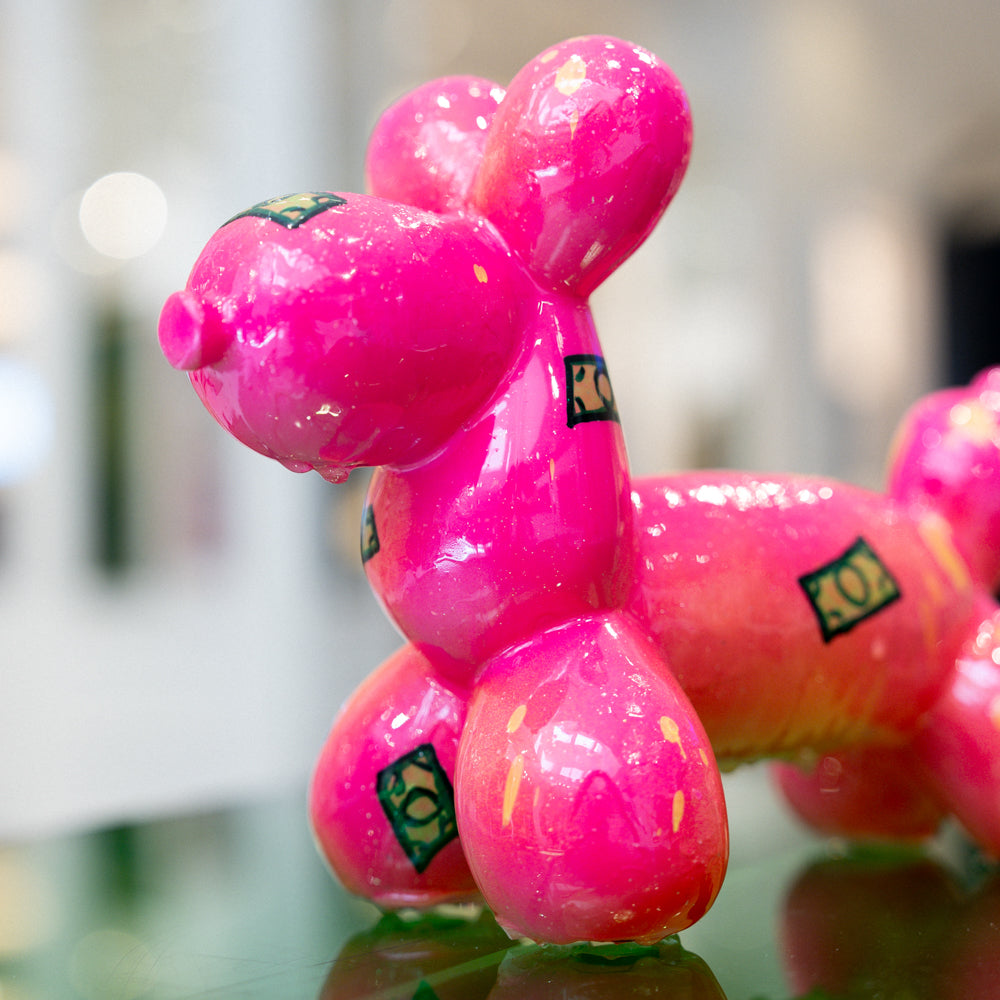 Pink balloon dog model on a reflective surface with a blurred background