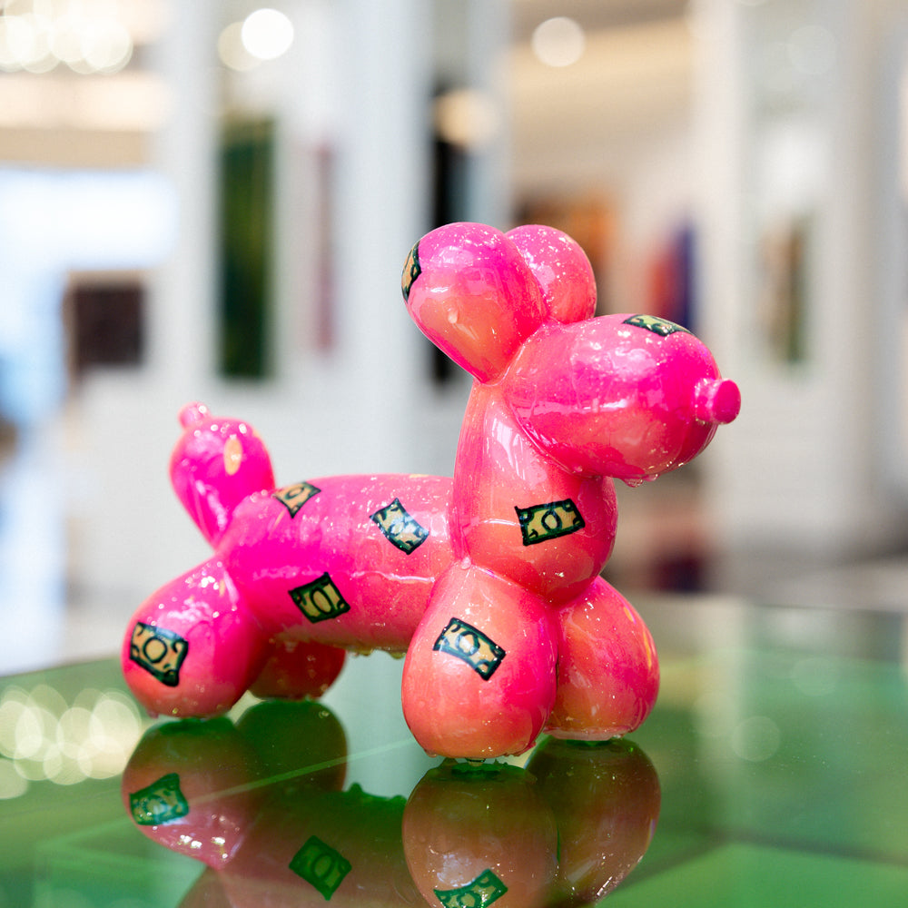 Pink balloon dog sculpture on a reflective surface with a blurred indoor background