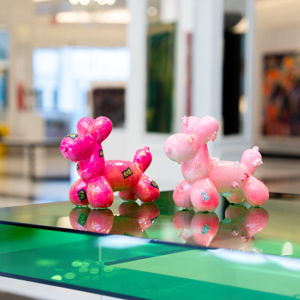 Pink balloon dog sculptures on a reflective surface with a blurred indoor background