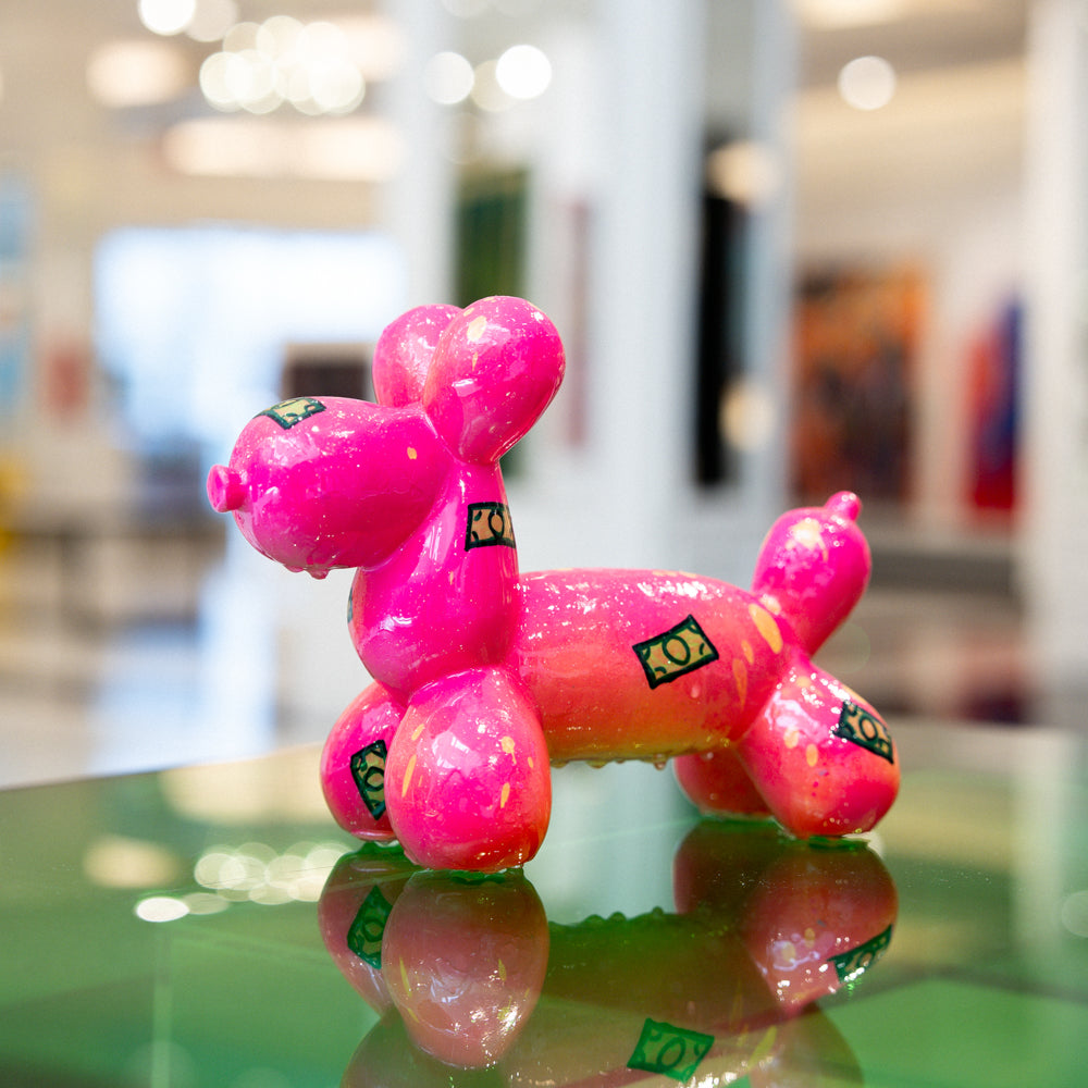 Pink balloon dog model on a reflective surface with a blurred indoor background