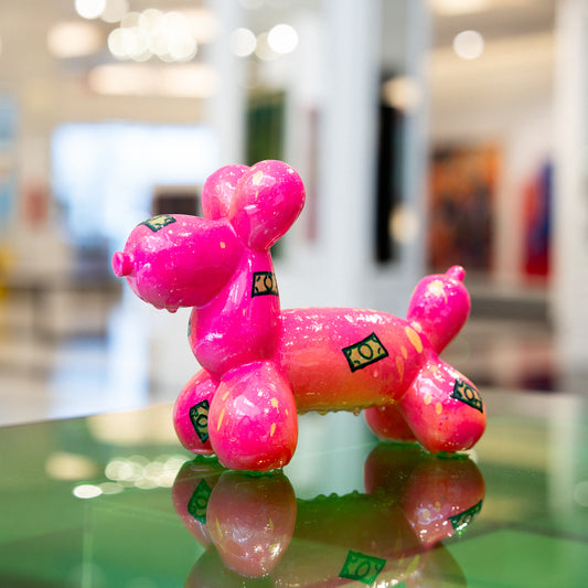 Pink balloon dog model on a reflective surface with a blurred indoor background